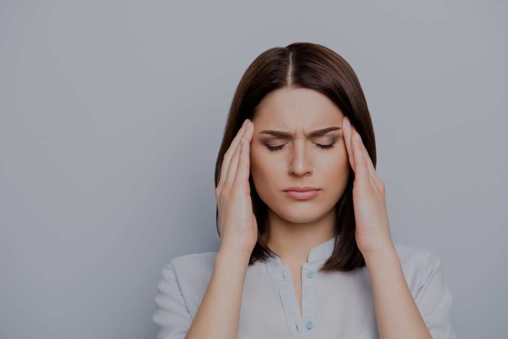 Portrait of upset, sad, pretty, nice, charming, stylish woman in shirt having head ache, stress, troubles, touching temples with fingers and close eyes, standing over grey background